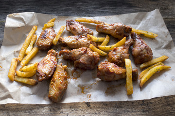 Appetizing fried pieces of chicken, pieces of chicken wings and fried potatoes located on paper and on an old wooden background