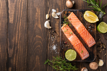 Flat lay with fresh raw salmon fillet and aromatic herbs, spices, pepper, salt, mushrooms lemon and rosemary. Old wooden background. Top view. Copy space.