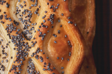 Baked bun with puff pastry, sprinkled with poppy seeds on a dark wooden background. Close-up. Food background.