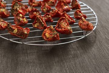 Sun-dried red tomatoes with garlic and Italian dried herbs on metal circle grid. Copy space for text. Homemade organic food.
