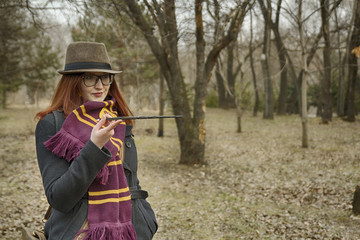 A witch girl with a magic wand in her hand, wearing glasses, a coat, a hat and a scarf, with a vintage bag, pronounces a spell