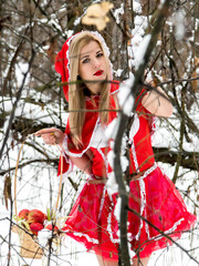 A girl in a red dress in a winter forest makes her way through the thickets. Little Red Riding Hood.