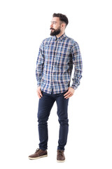 Confident relaxed bearded handsome fashion model in plaid shirt with thumbs in pockets looking away. Full body isolated on white background.