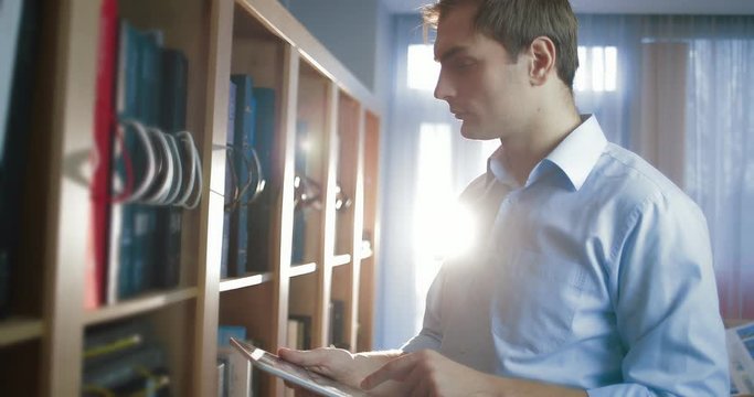 Businessman uses a tablet computer standing next to a large shelf