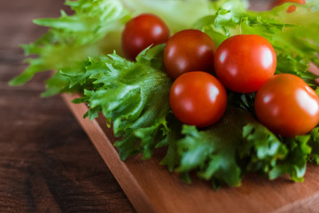 Cherry tomatoes and salad leaves on the cutting board with soft focus on the background. Top view. Copy text space. 