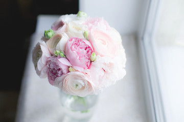 Gorgeous bridal bouquet of pink peonies Sarah Bernhardt, ranunculus Hanoi, Keira roses by David Austin and white Eustoma on the window background. Wedding floristry