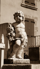 Statue of Bacchus (Dionysus) with grapes in his hands against rough stone wall. Garden sculpture. (Provence, France). Sepia photo.