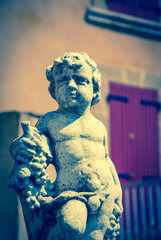 Statue of Bacchus (Dionysus) with grapes in his hands against rough stone wall. Garden sculpture....