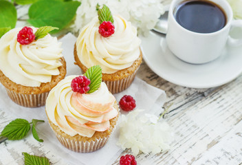 Delicate vanilla cupcakes with cream and raspberries on a white wooden background