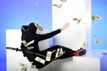 back view of ninja in black clothing catching dollar banknotes on white blocks isolated on blue © LIGHTFIELD STUDIOS