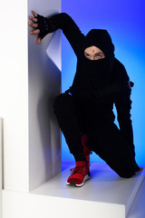 ninja in black clothing with katana behind standing on white block isolated on blue