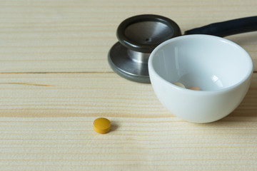 A tablet and pills in a white cup and stethoscope