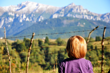 Back side portrait of a kid in focus, blonde girl with short hair, looking to the mountains