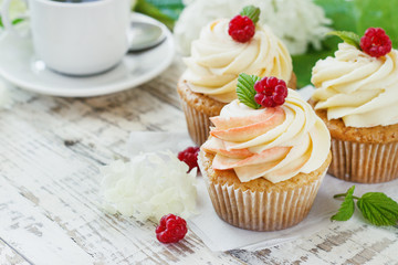 Delicate vanilla cupcakes with cream and raspberries on a white wooden background