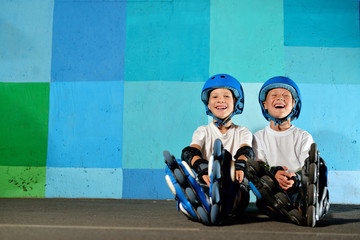 Yong little athletic boys on roller sitting against the blue graffiti wall © katyshka