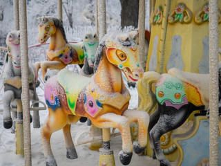 carousel with multicolored horses covered with snow in winter