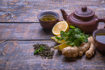Tea cup, tea pot and slices of lemon, ginger, mint, on wooden background