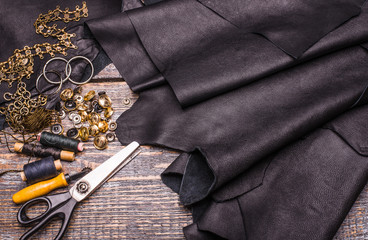 Black leather texture, rivets, buttons, scissors, threads on wooden background, surface