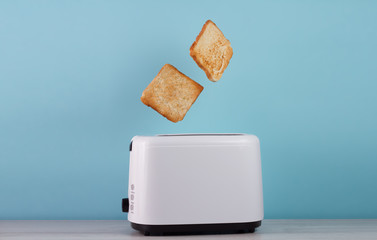 Roasted toast bread popping up of stainless steel toaster on a blue backgroun.