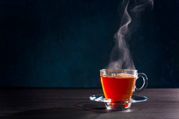 Freshly brewed black tea in a transparent glass Cup,escaping steam,darker background.