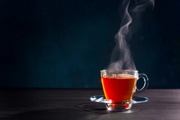 Deurstickers Vers gezette zwarte thee in een transparante glazen beker, ontsnappende stoom, donkerdere achtergrond. © OlegKovalevich