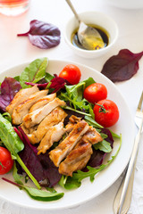 Sliced grilled chicken with green leaves salad on white plate