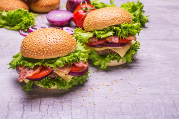 Craft beef burger and fresh vegetables, tomatoes, onion, salad, cheese,  on wooden table isolated on gray background.