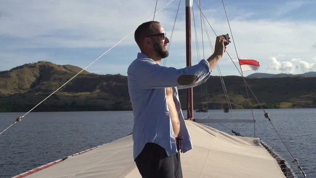 Young man taking photos with cellphone sailing yacht, super slow motion
