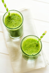 Healthy green smoothie made from spinach, apple and cucumber in a jars with red straw on white wooden table