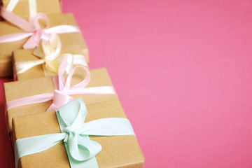 Simple composition with multiple presents wrapped in hand made blank craft paper gift wrap, pastel satin bow. Simple giftbox, wrapping, giftwrap, silk ribbon. Pink background, close up, copy space.