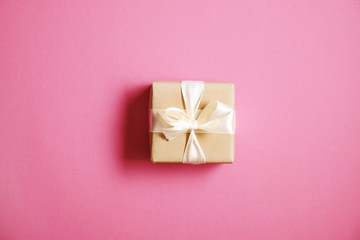 Single present wrapped in hand made craft paper gift wrap, tied w/ pastel satin bow. Giftbox, brown wrapping, giftwrap, yellow ribbon. Holiday concept. Close up, pink background, copy space, top view