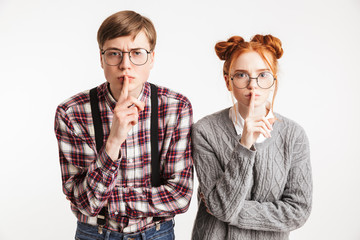 Serious couple of school nerds showing silence gesture