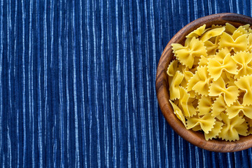 farfalle macaroni pasta in a wooden bowl on a striped white blue cloth background with a side. Close-up with the top. With space for text.