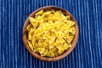 farfalle macaroni pasta in a wooden bowl on a striped white blue cloth background in the center. Close-up with the top.