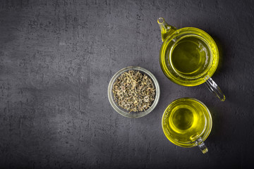Green tea,brewed in a transparent teapot.Dry tea leaves, dark black background.The view from the top.