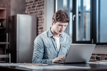 Business correspondence. Handsome confident skillful man sitting at table while typing and looking at screen