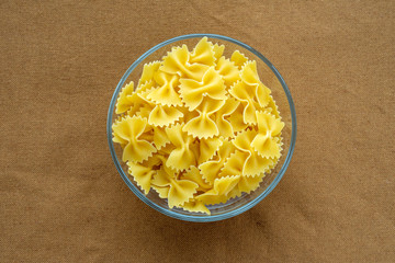 farfalle macaroni pasta in a glass bowl on a brown rustic texture background, in the center close-up from the top.