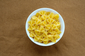 farfalle macaroni pasta in a white cup on a brown rustic texture background, in the center close-up from the top.