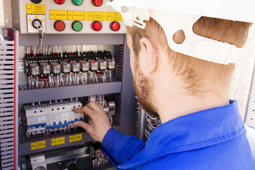 electrician working in white helmet switches the switch in the electrical cabinet. The engineer works in industrial electrical cabinet.