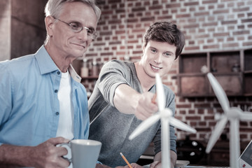 Two generations. Satisfied glad male engineers staring at windmills model while working together and sharing thoughts