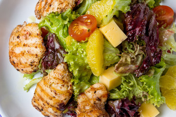 Juicy salad with chicken steak, salad mix, cherry tomatoes, orange, cheese. Under the olive oil. In a round plate. View from above. Close-up