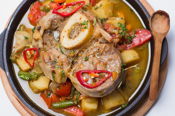 Steak Osso Buco. With stewed vegetables: potatoes, bell peppers, carrots, onions, greens. View from above. White background. Close-up