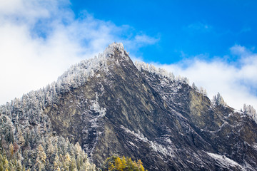 massive Bergspitze in der Schweiz im Winter, schneebedeckt, mit verschneiten B&auml;umen im Wald und blauer Himmel mit ein wenig Wolken
