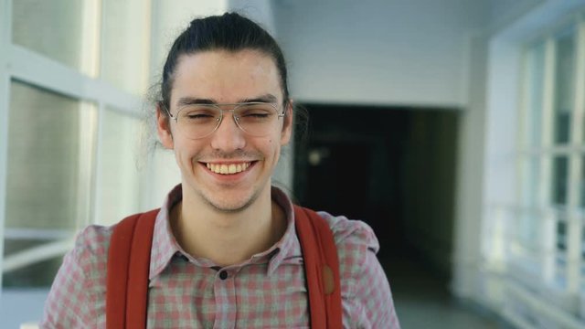 Portrait of young handsome attractive male student of caucasian ethnicity standing in wide white hallway indoors looking at camera and smiling positively