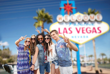 summer holidays, vacation, tourism and travel concept - group of smiling hippie friends taking selfie by smartphone and showing peace over welcome to fabulous las vegas sign background