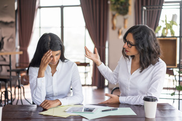 Disappointed business woman scolding colleague. They are sitting at table in cafe. Accusation of...