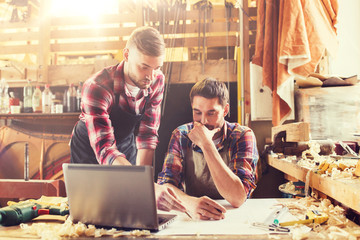 profession, carpentry, technology and people concept - two carpenters with laptop computer and blueprint at workshop