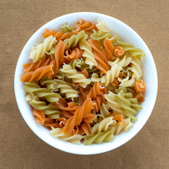 Multicolor spiral macaroni pasta in a white cup on a brown rustic texture background, in center close-up from the top.