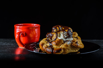chocolate eclair on a black plate and coffee in a red mug on a dark background