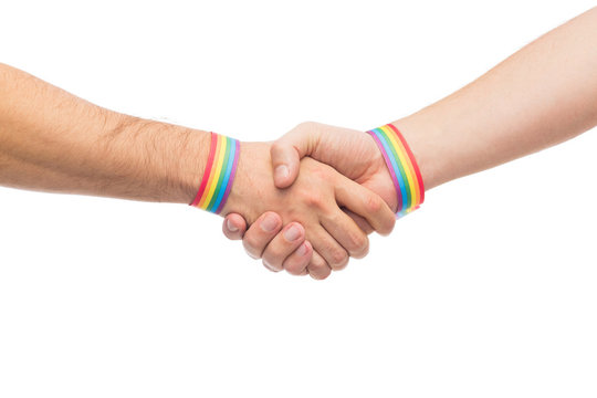lgbt, same-sex love and homosexual relationships concept - close up of male couple hands with gay pride rainbow awareness wristbands making handshake